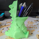 3D printed dinosaur pencil holder in green holding pencils and pens on desk